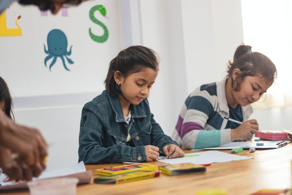 Photo of two students working in classroom, they have various writing tools on the table and are focused on their own individual work. How this relates to accessibility is written below.